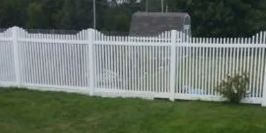 A white picket fence surrounds a grassy yard with a small shed in the background.