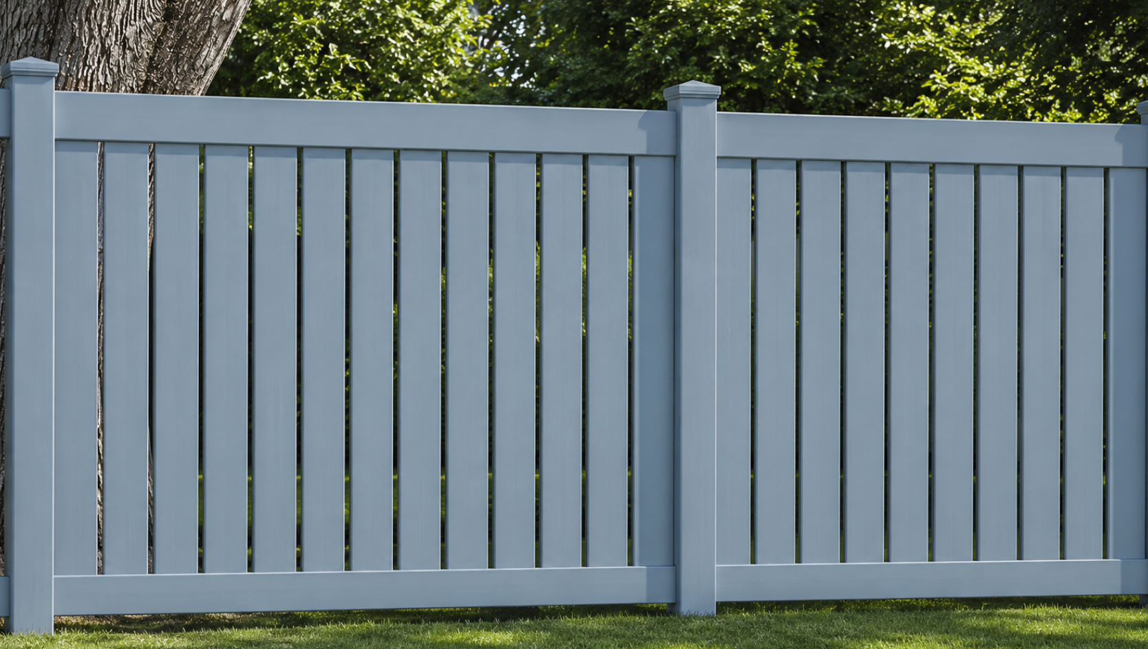 A pale blue vertical slat fence stands on green grass with trees visible behind it.