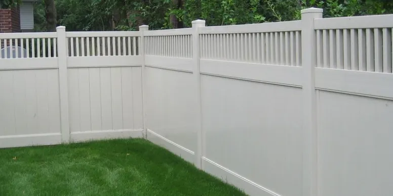 White vinyl privacy fence with vertical slats on top and solid panels below, enclosing a corner of a green grassy yard.