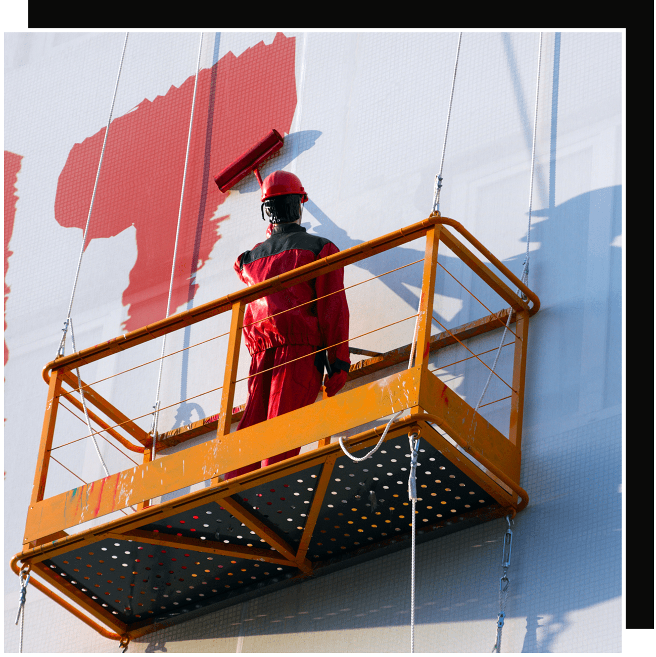 Painter on suspended orange platform painting wall