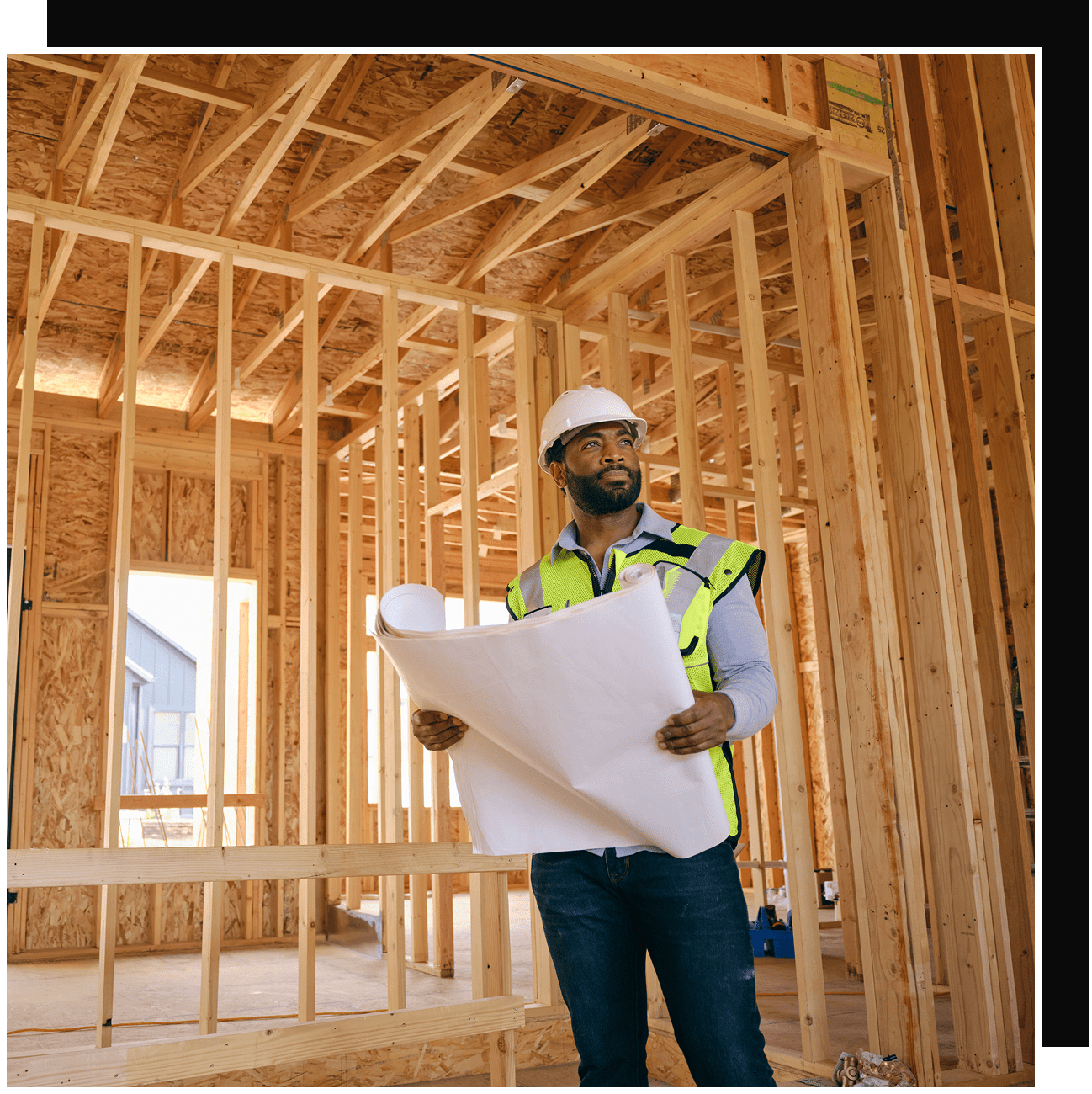 Contractor inspecting house framing with blueprints