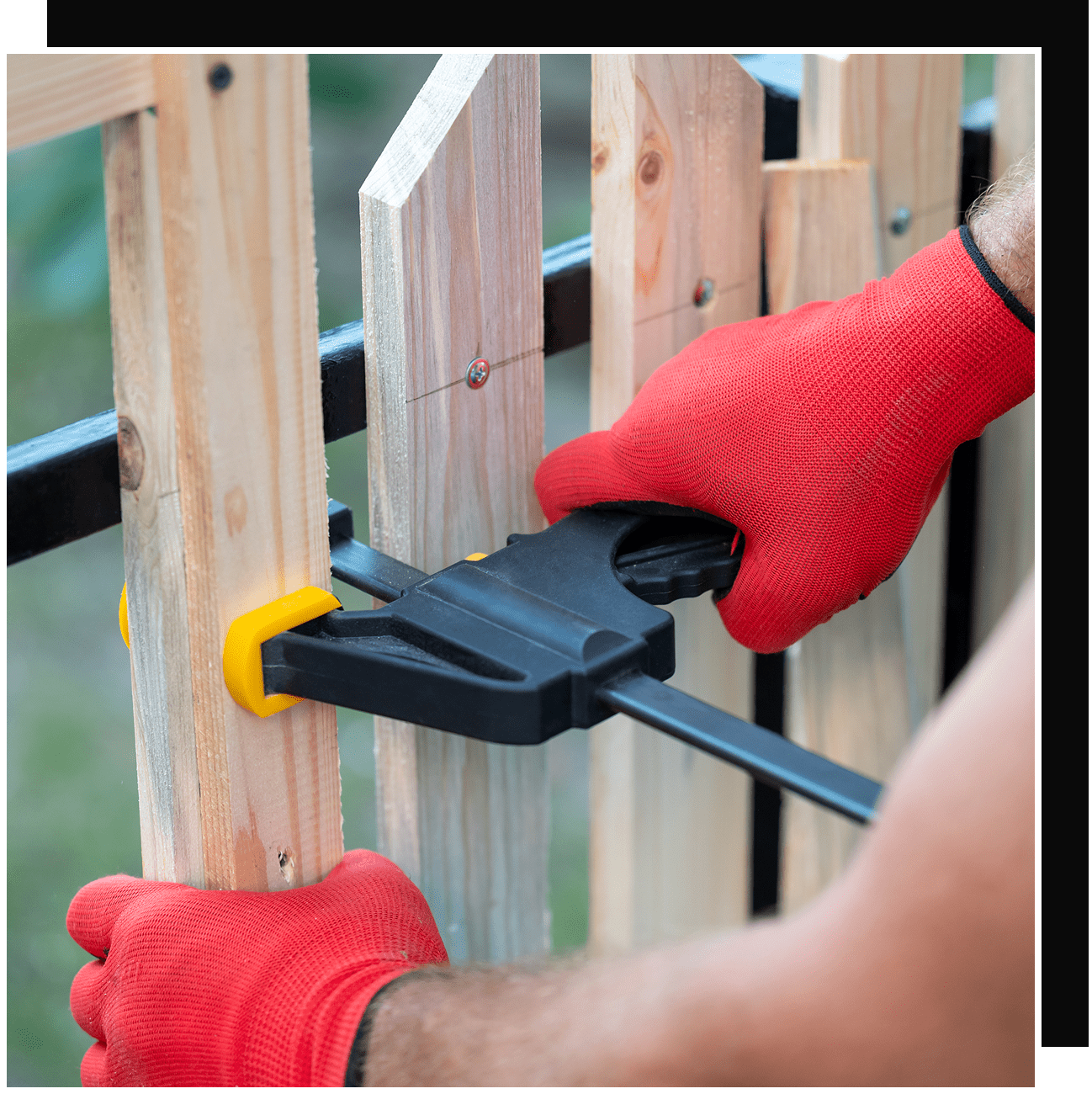 Hands in red gloves clamping wooden fence slats