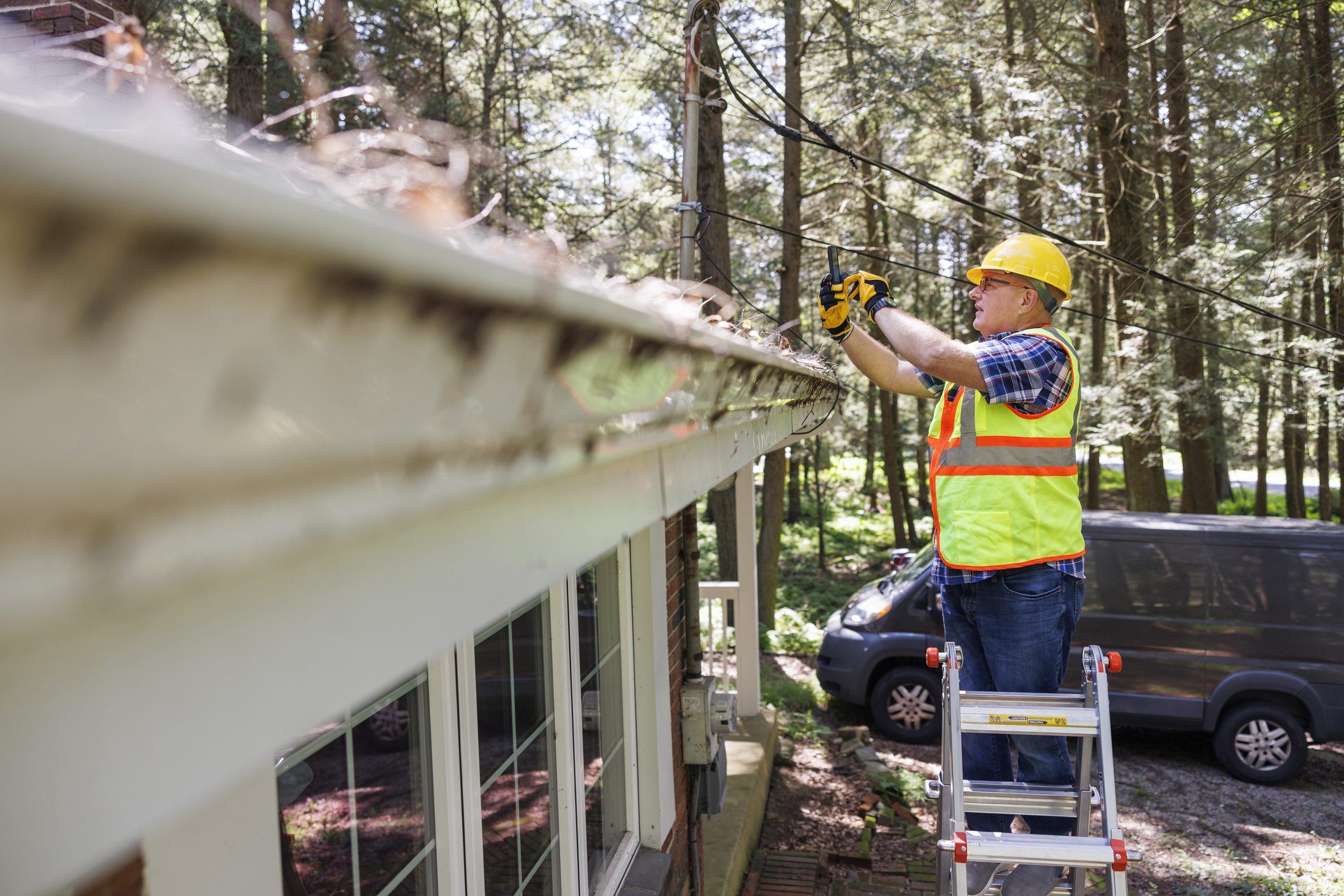 Worker cleaning home gutters from ladder