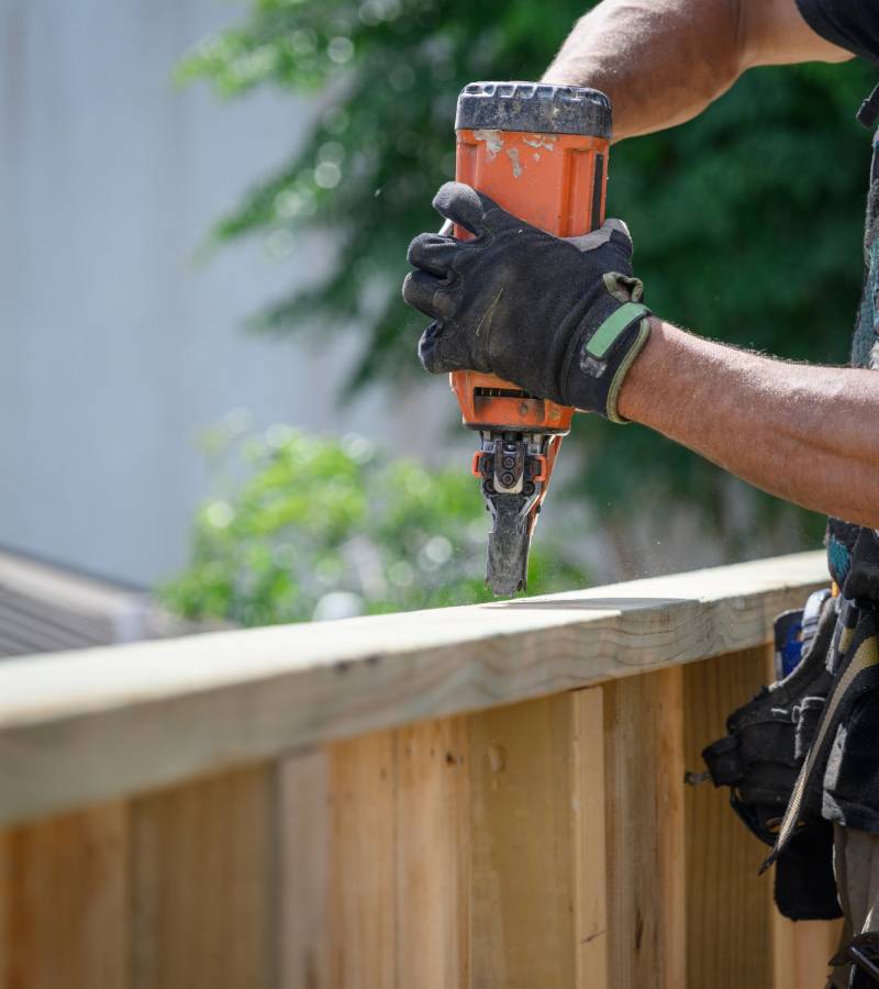 Gloved hands using nail gun on deck railing