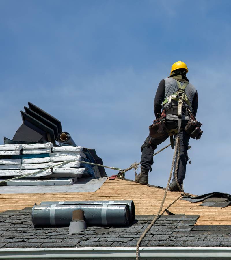 Roofer installing shingles wearing safety harness