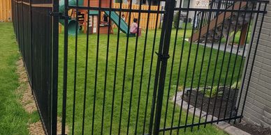 Black metal fence gate enclosing backyard playset