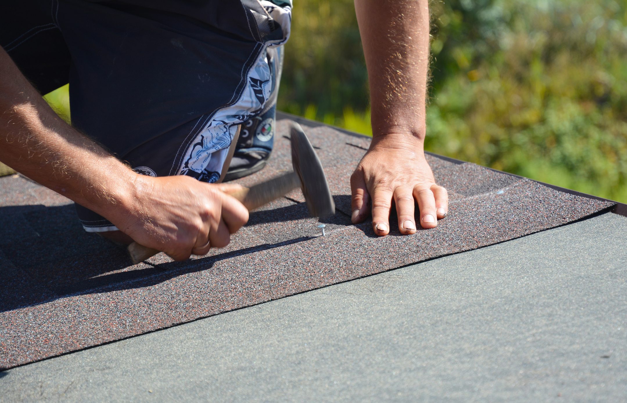 Roofer installing asphalt shingles on house construction roof corner with hammer and nails. Roofing construction. Roofing contractor installing roof tiles.