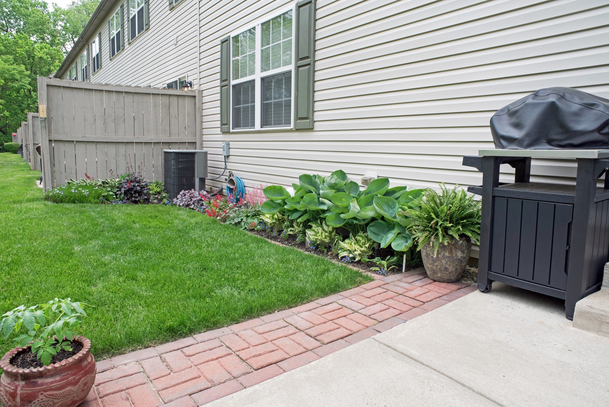 View of back yard garden area of modern condo with grill and red brick pavers.