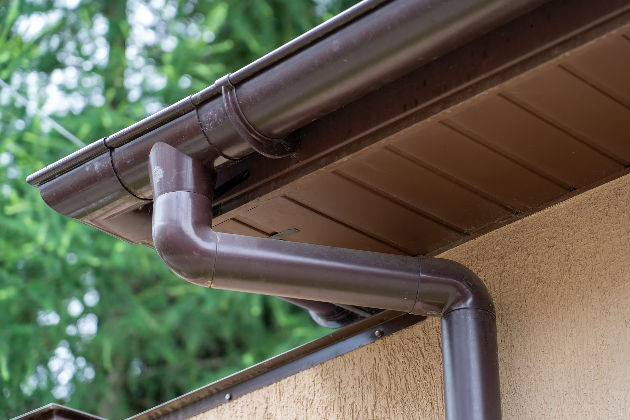 Brown plastic gutter system against green trees, roof overhang