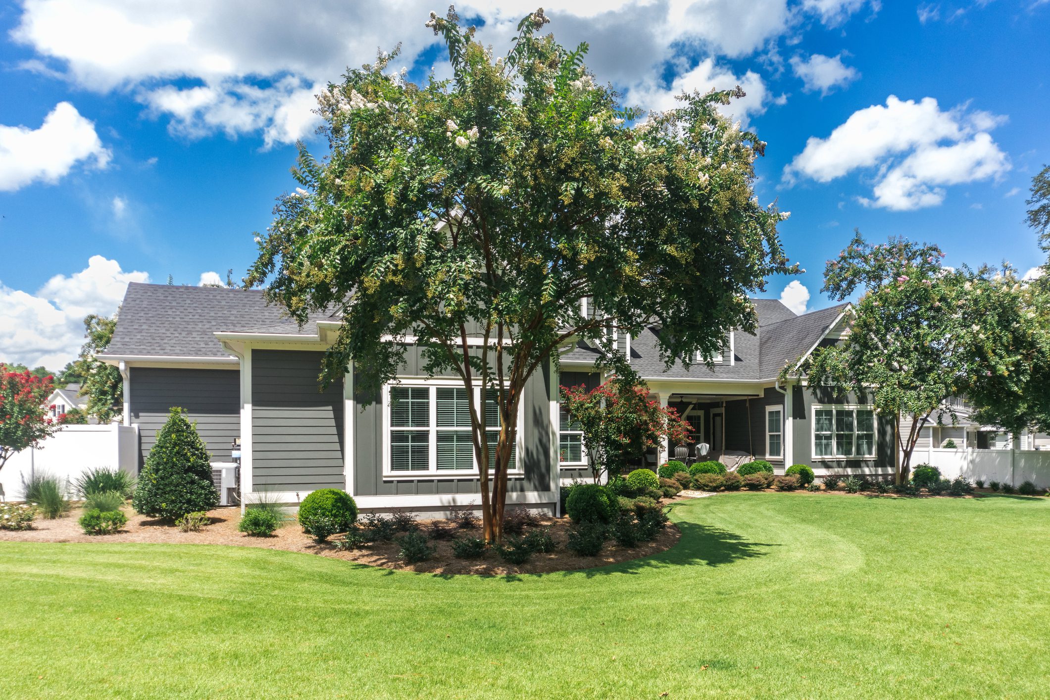 The side view of the backyard of a large gray craftsman new construction house with a landscaped yard.