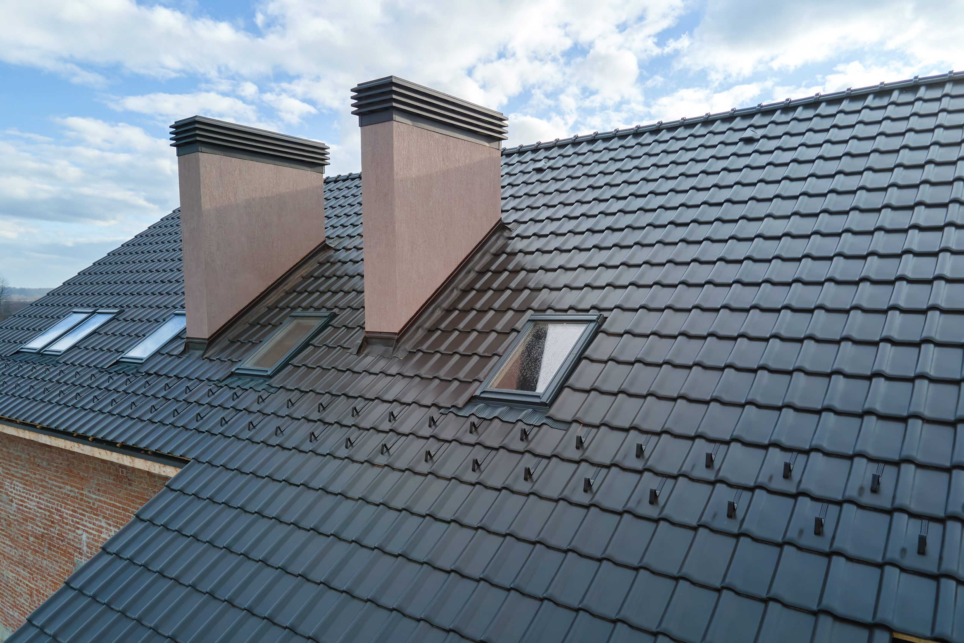 Closeup of attic windows and brick chimneys on house roof top covered with ceramic shingles. Tiled covering of building.