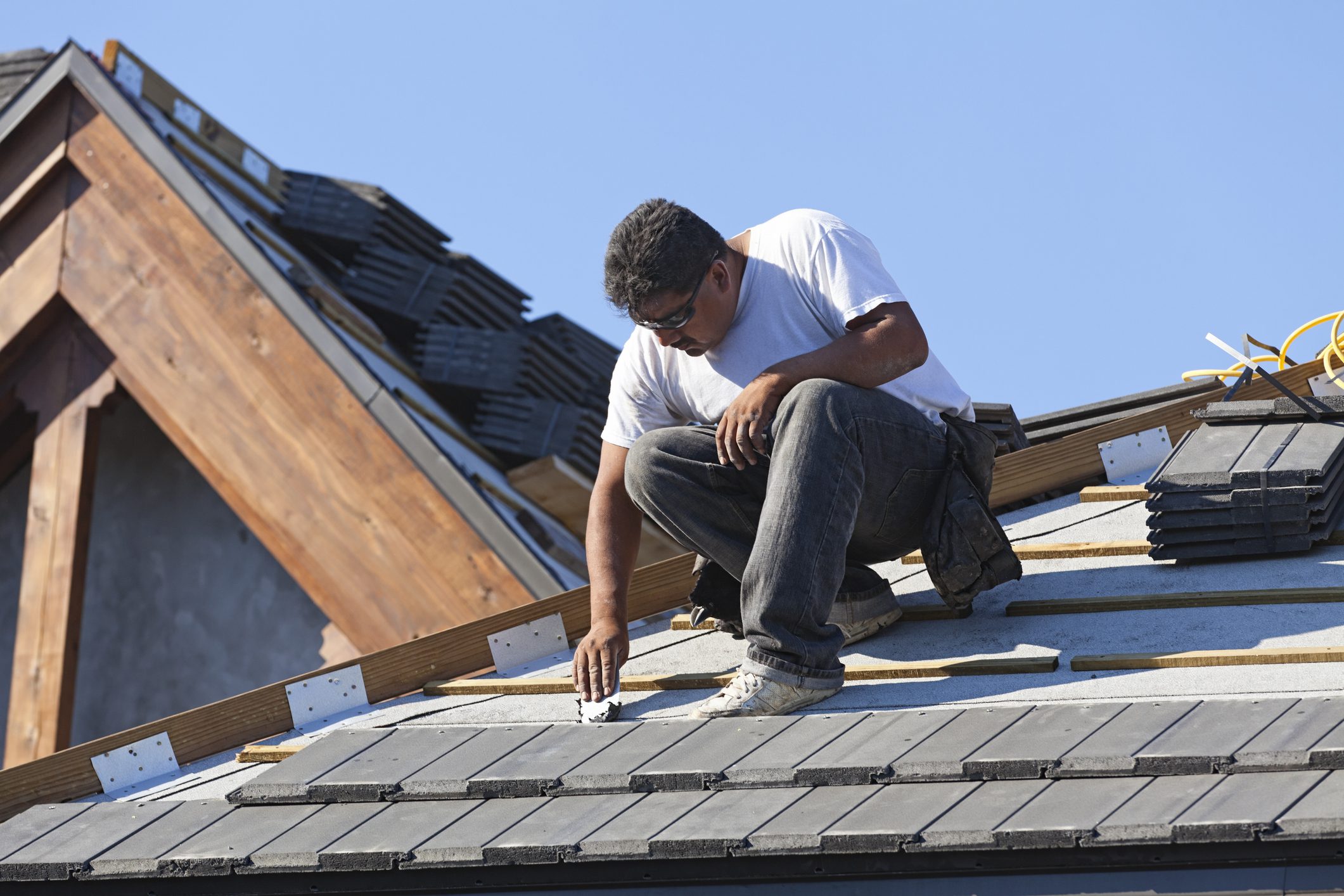 A roofer patches a nail hole in a new roof before tile is laid down.