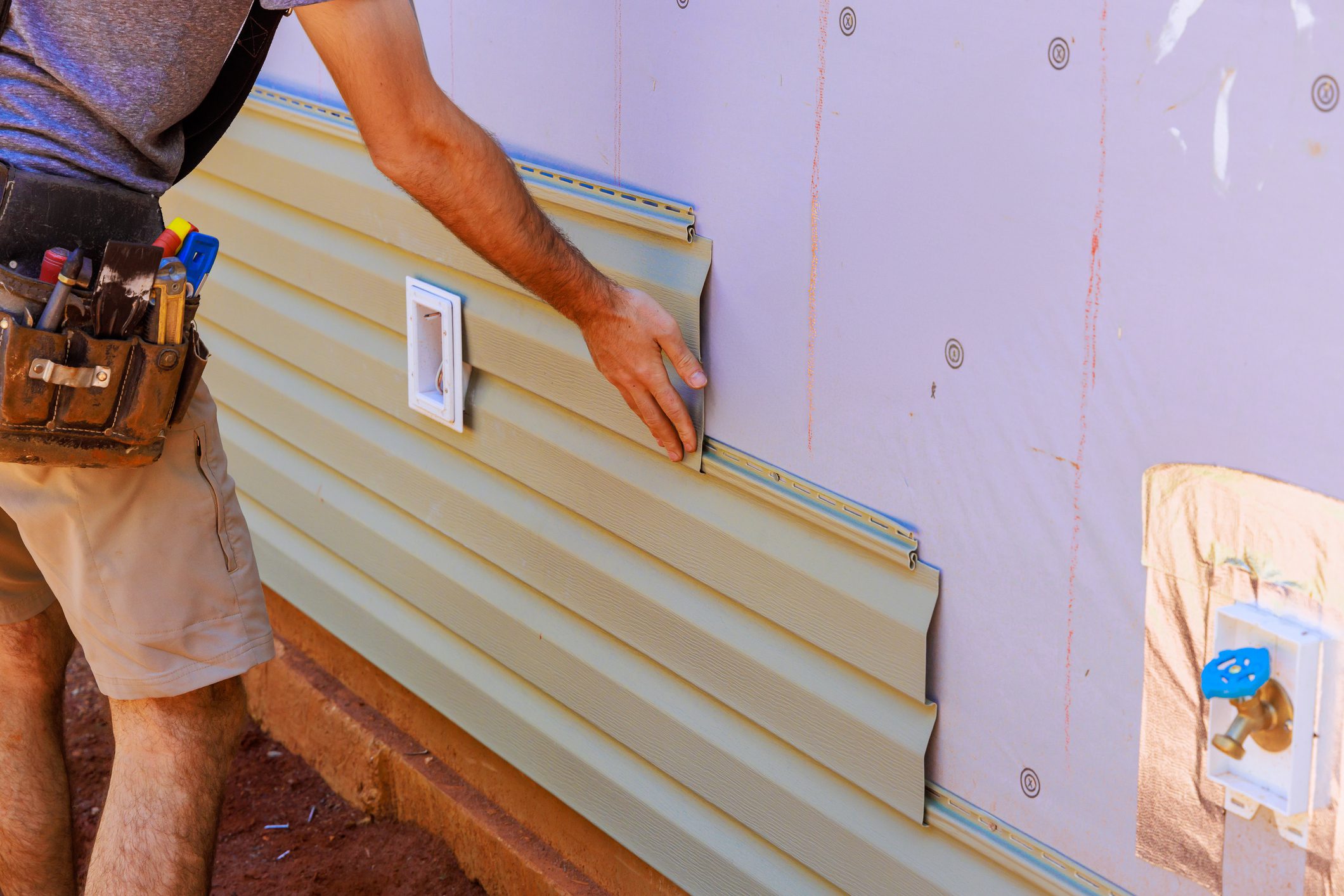 An employee installs vinyl plastic siding panels on wall facade of new residence