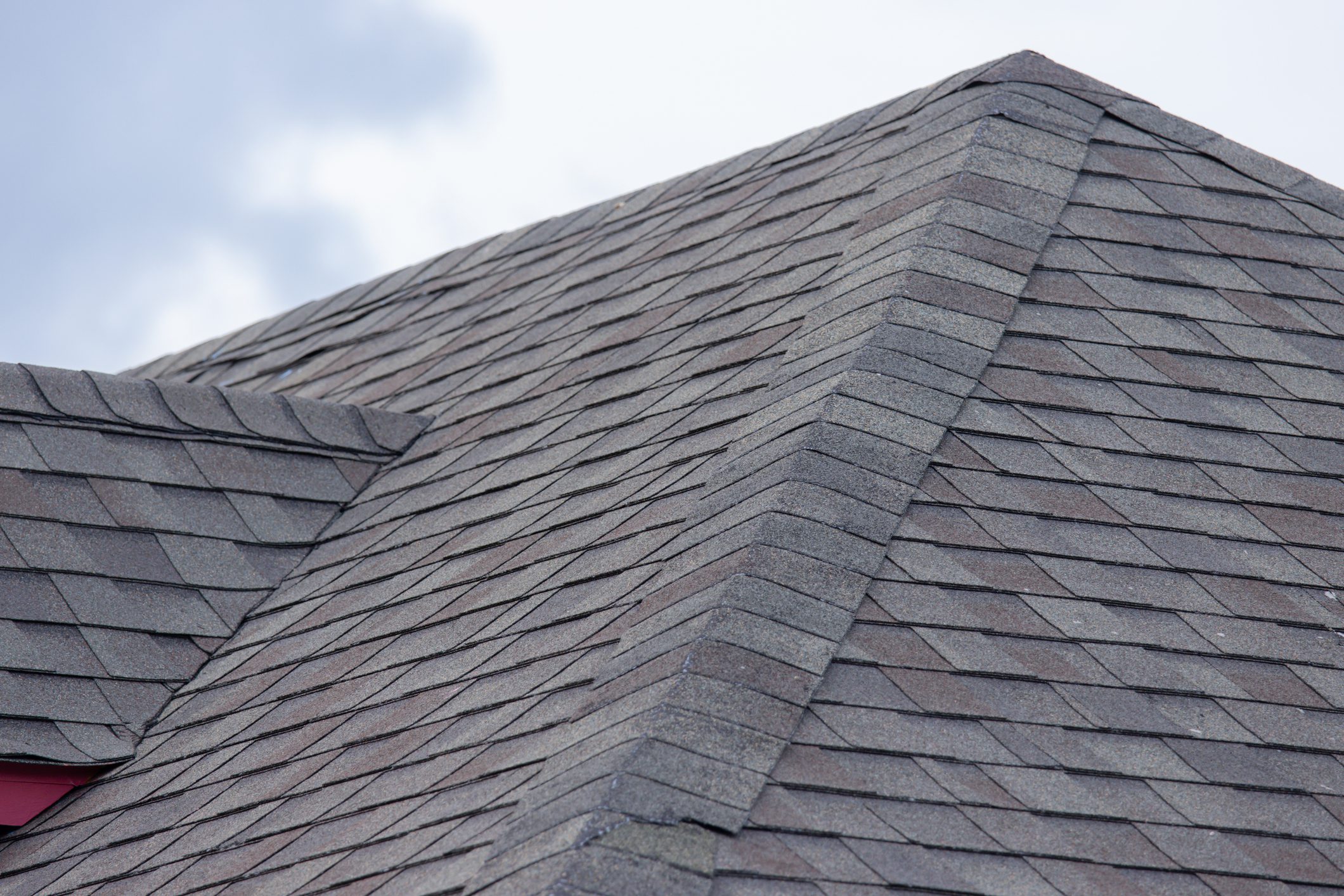 A roof with a gray and tan shingle. The roof is slanted and has a red trim