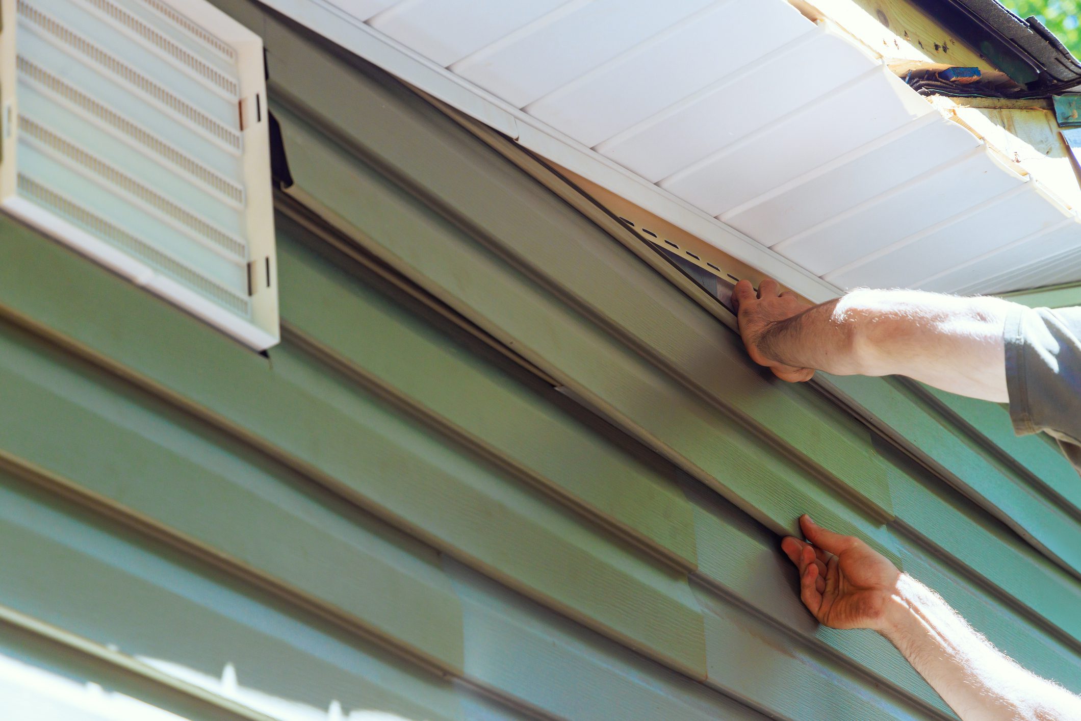 Construction employee installs vinyl plastic siding panels on new house wall facade
