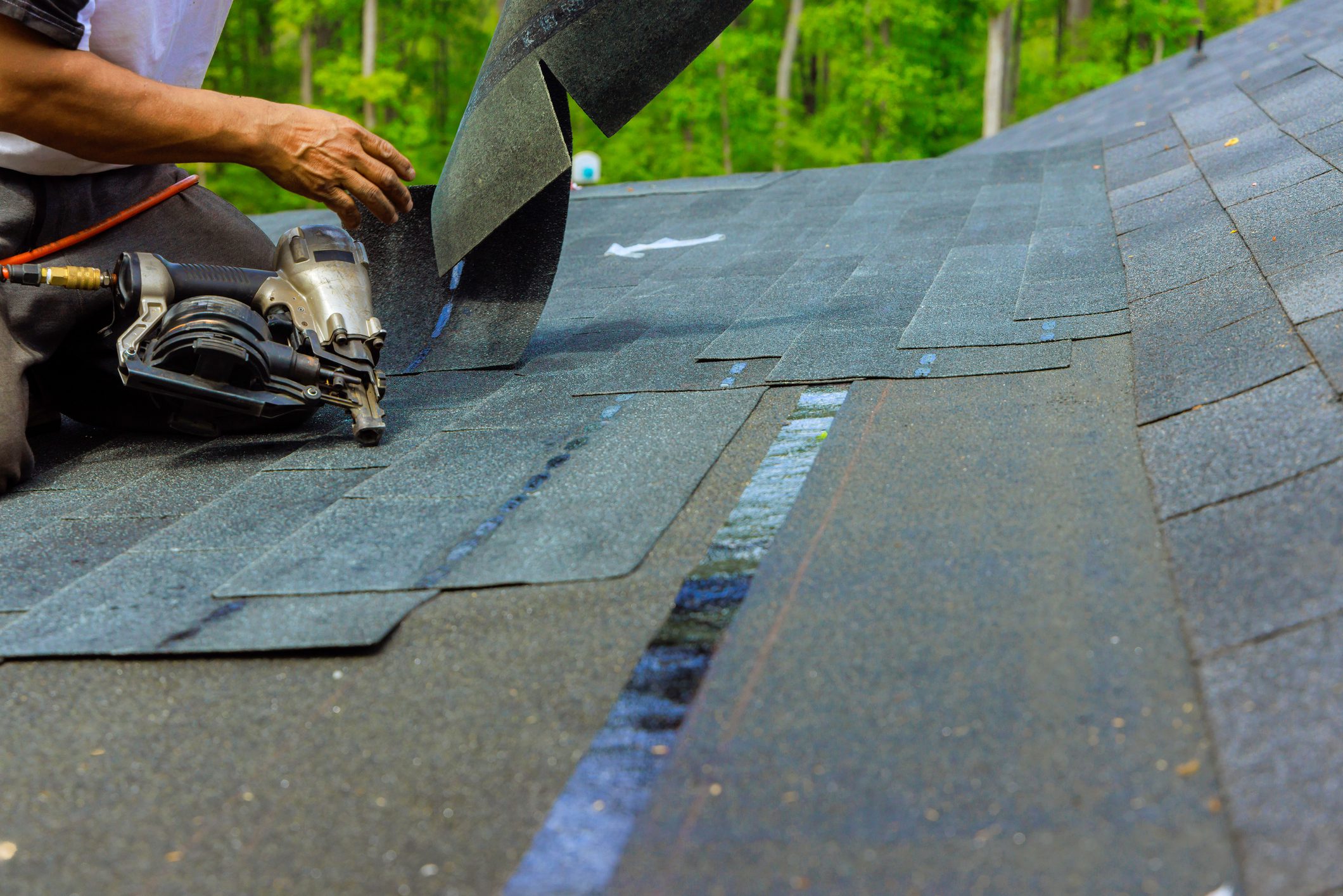 Construction worker installed new bitumen shingles on roof with an air pneumatic nail gun