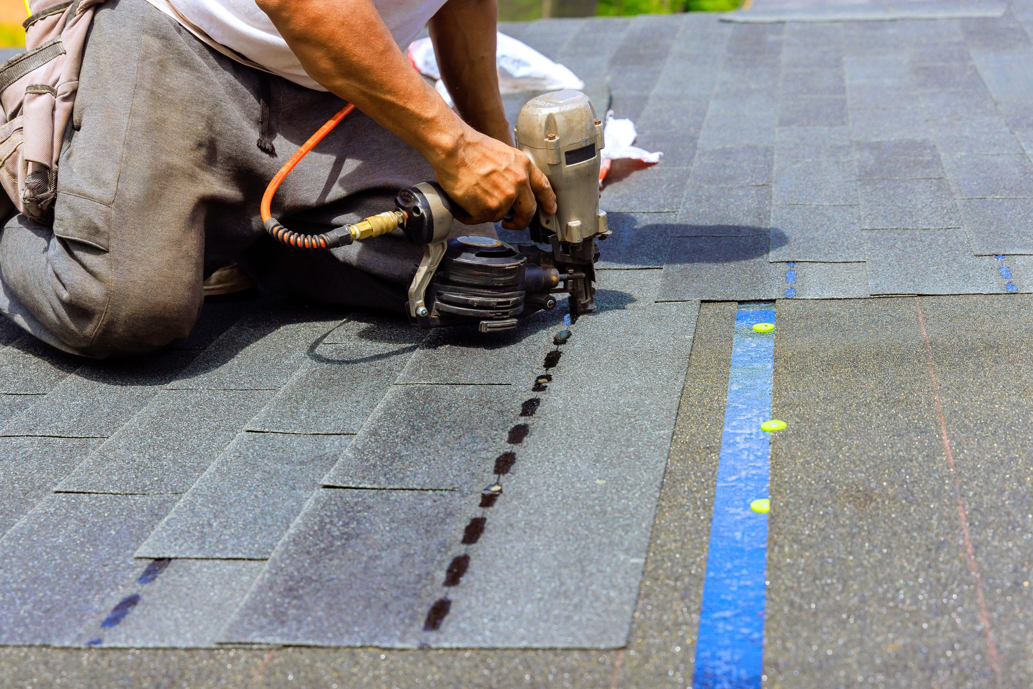 As roofer was installing new bitumen shingles on roof, construction worker used an air pneumatic nail gun