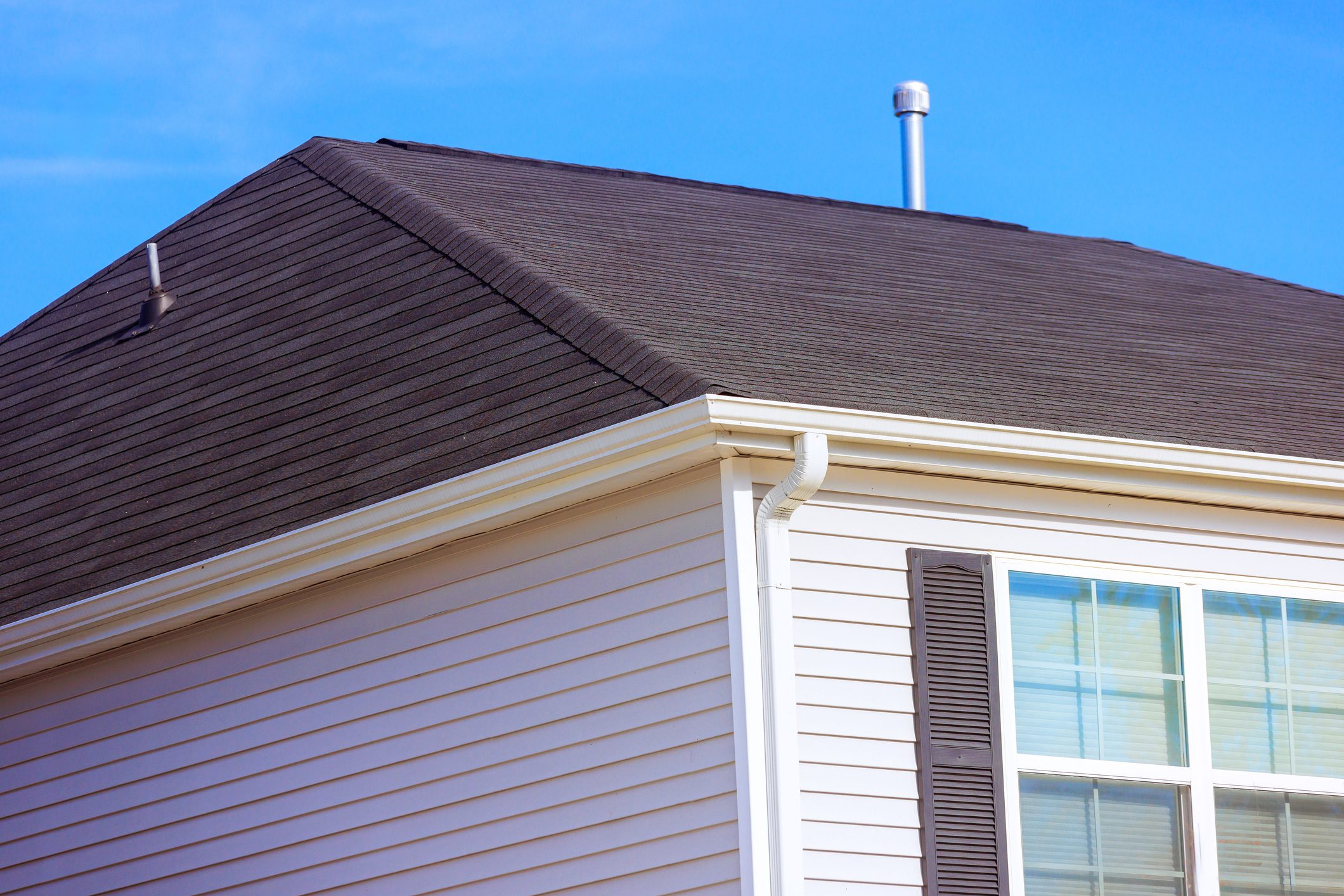Well maintained residential roof featuring asphalt shingles, white siding home displays neat gutters, window frames, indicating care