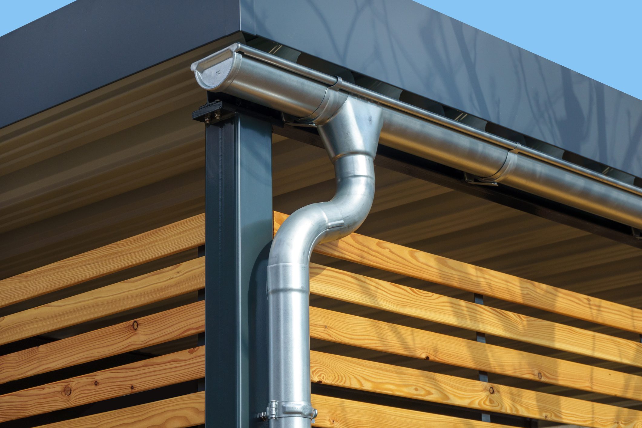 Gutter and downpipe on a modern carport with metal roof and wooden slat wal