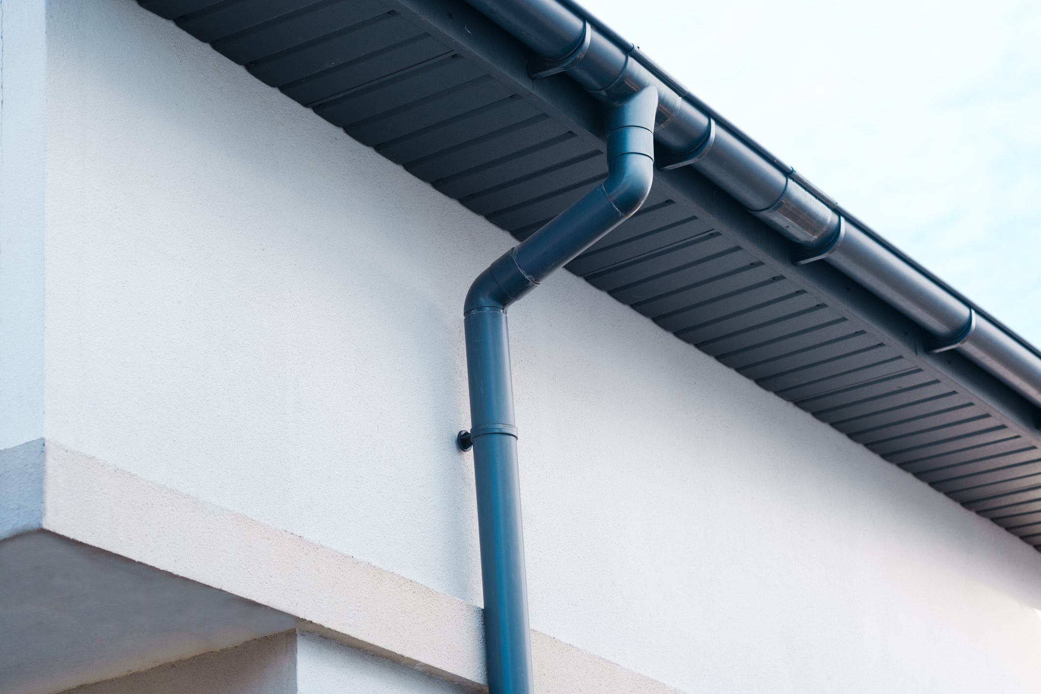Dark gray gutter system attached to white building structure under clear sky.