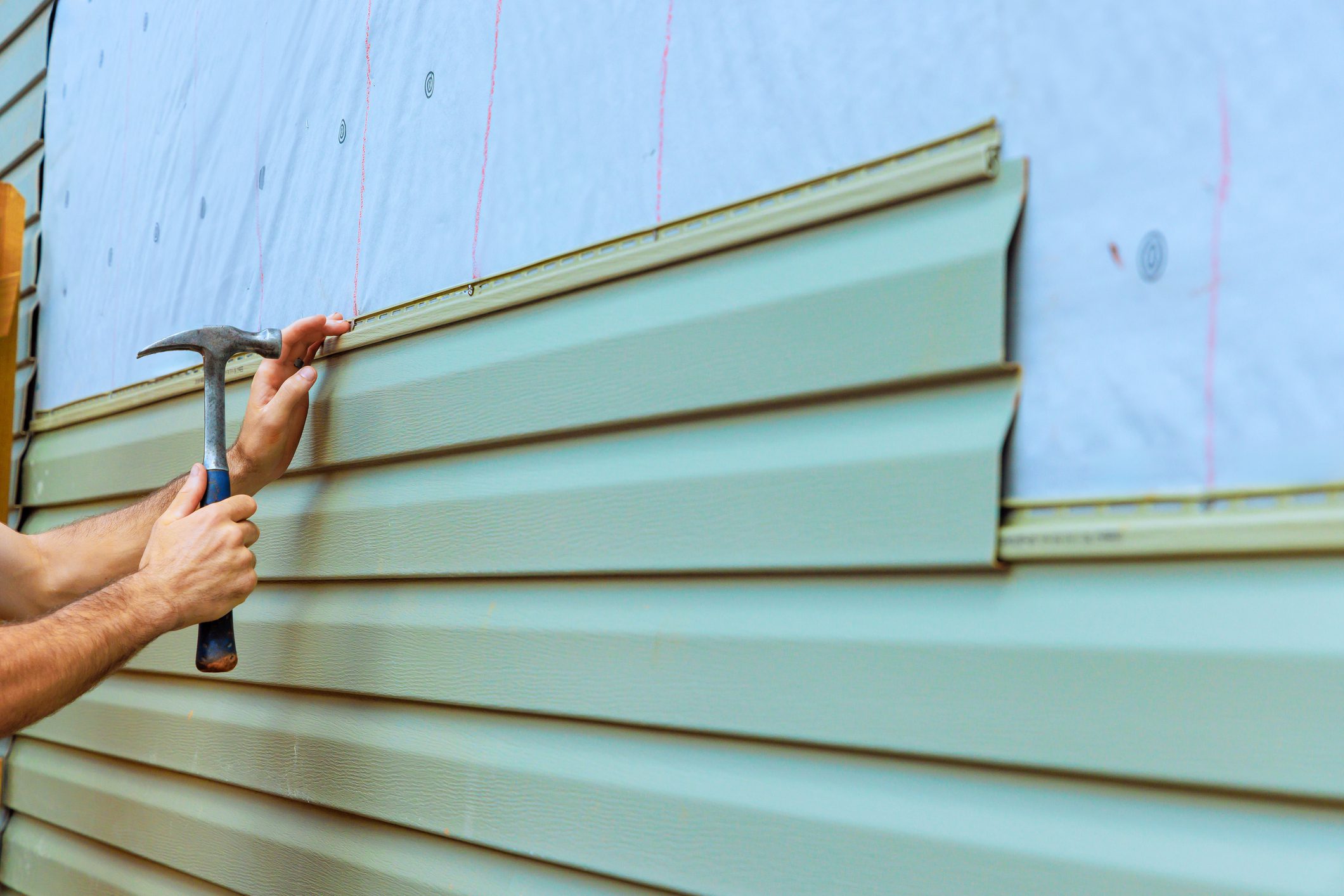 Contractor is installing new siding on house exterior, carefully aligning, hammering panels into place.