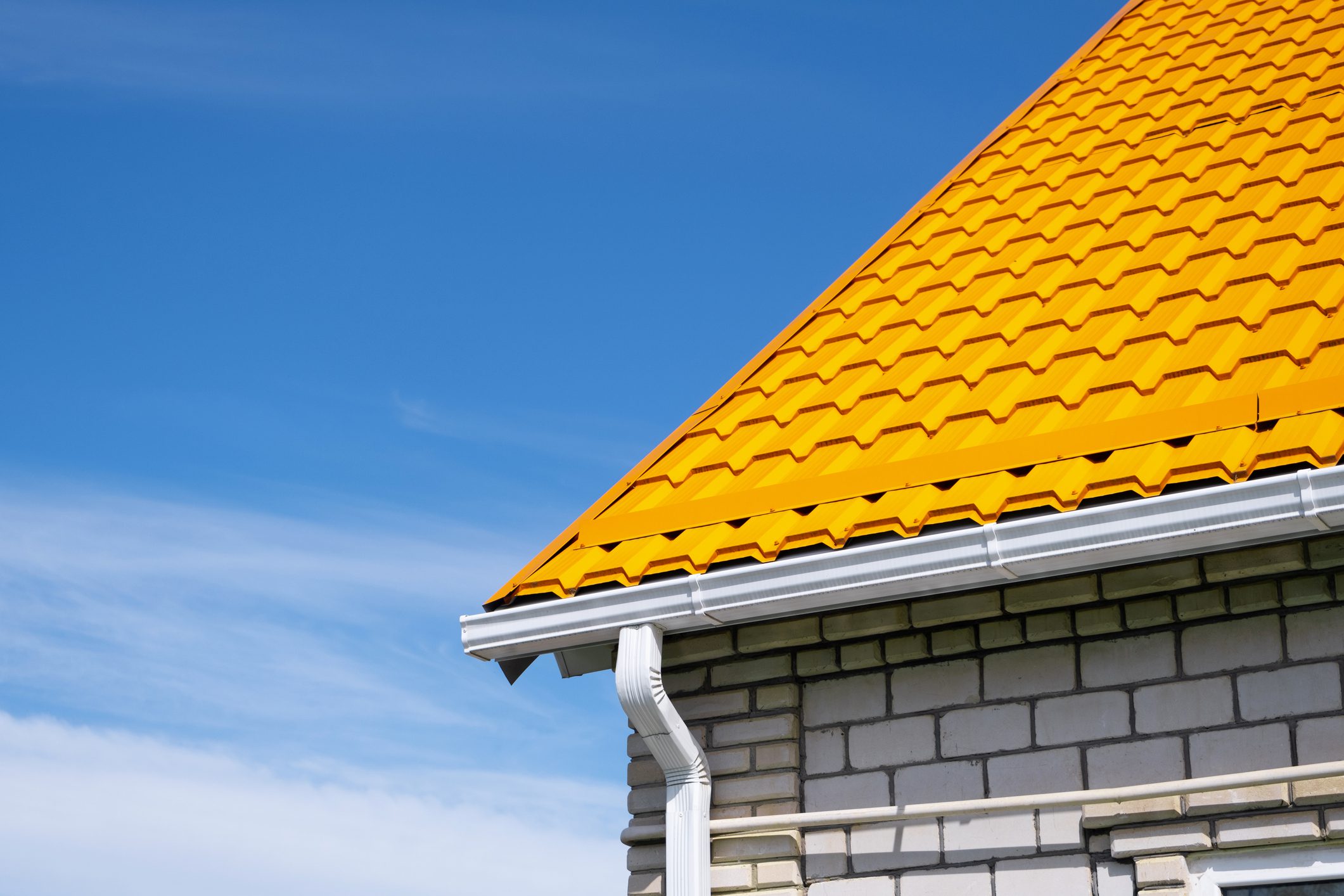 Rain Gutter Pipeline System on brick house , bright yellow metal tile roof against blue sky