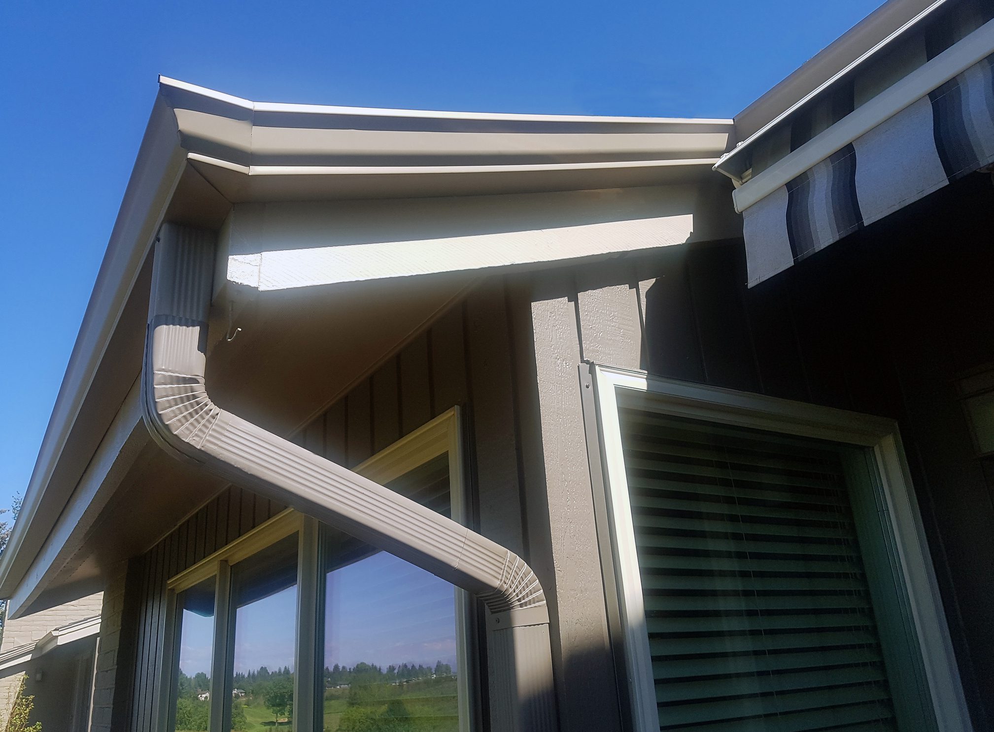Exterior of Rooftop of home showing gutter, galvanized drain pipe,eaves trough and Soffit. Windows below with reflection.