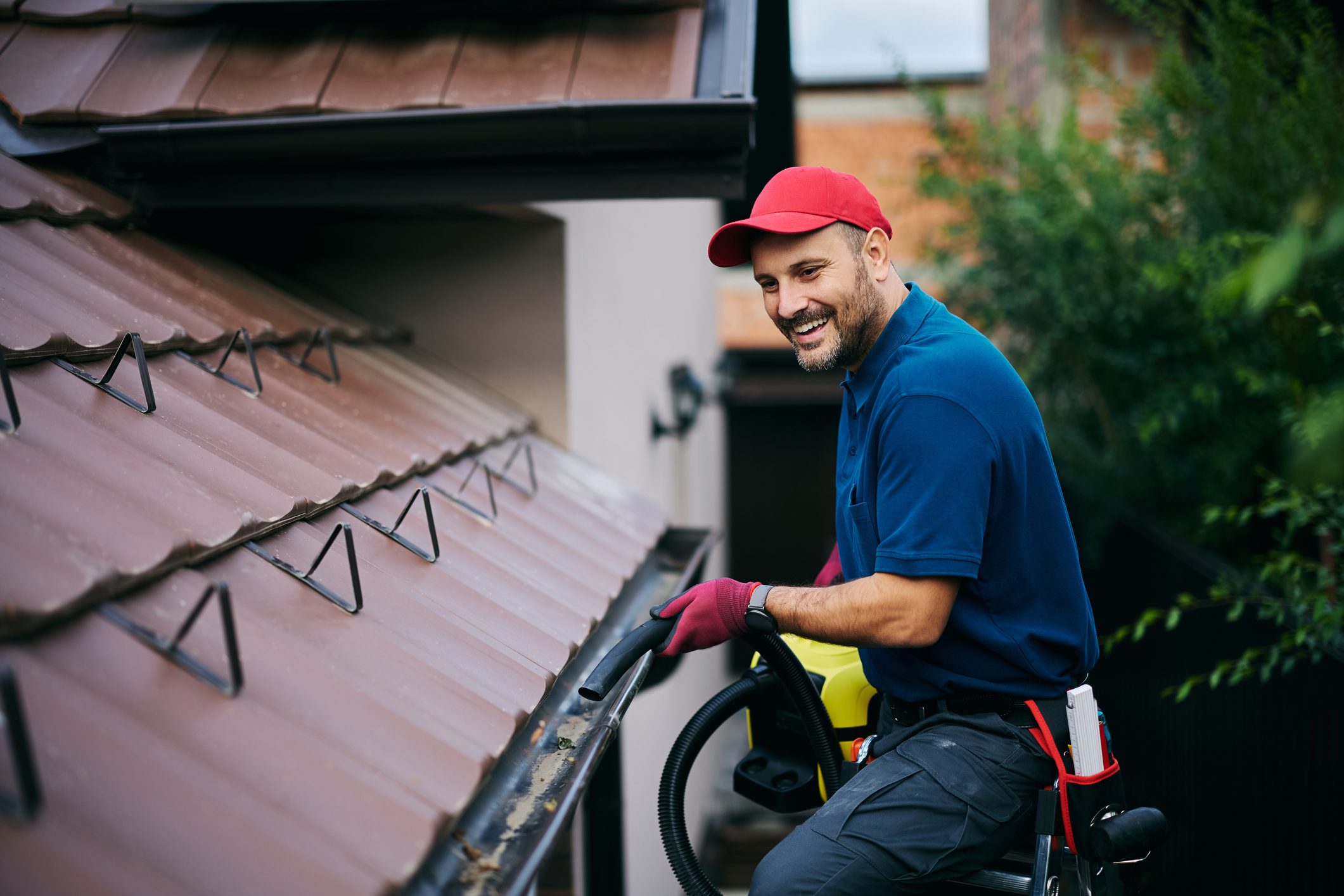 Happy man using leaf blower while cleaning gutters on the roof of a house. Copy space.