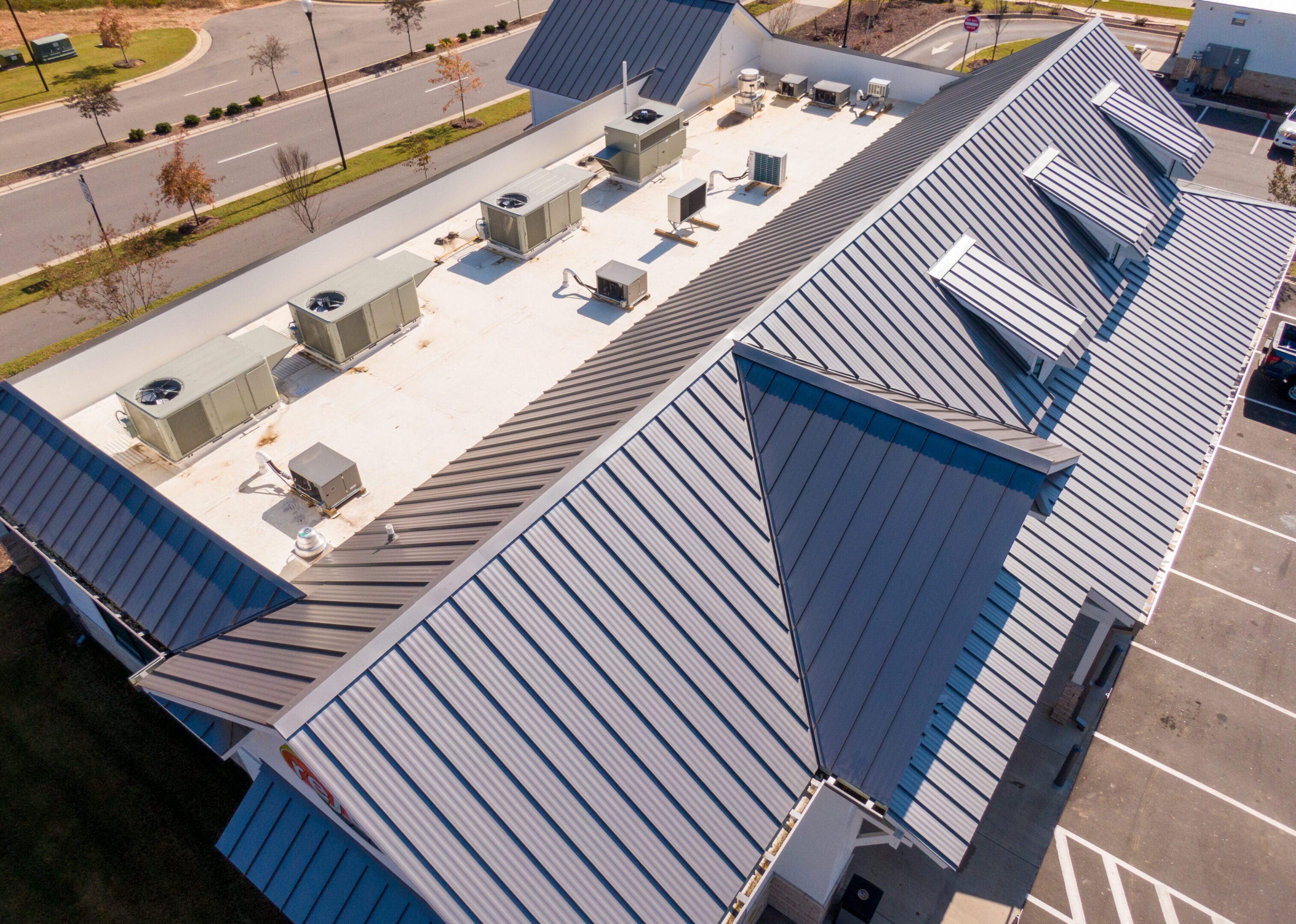 Drone aerial photos showcasing commercial buildings with sleek standing seam metal roofs. The images highlight the reflective steel panels, clean architectural lines, and durable construction used in contemporary retail and industrial facilities. Captured under bright sunlight, emphasizing the modern design and energy efficiency of metal roofing systems.