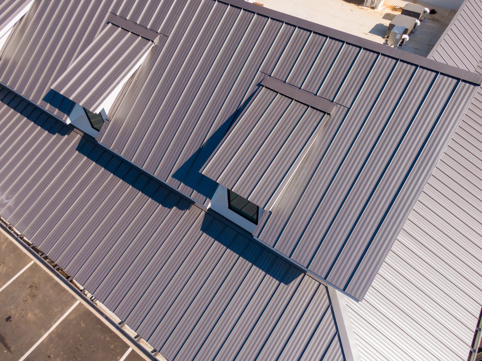 Drone aerial photos showcasing commercial buildings with sleek standing seam metal roofs. The images highlight the reflective steel panels, clean architectural lines, and durable construction used in contemporary retail and industrial facilities. Captured under bright sunlight, emphasizing the modern design and energy efficiency of metal roofing systems.