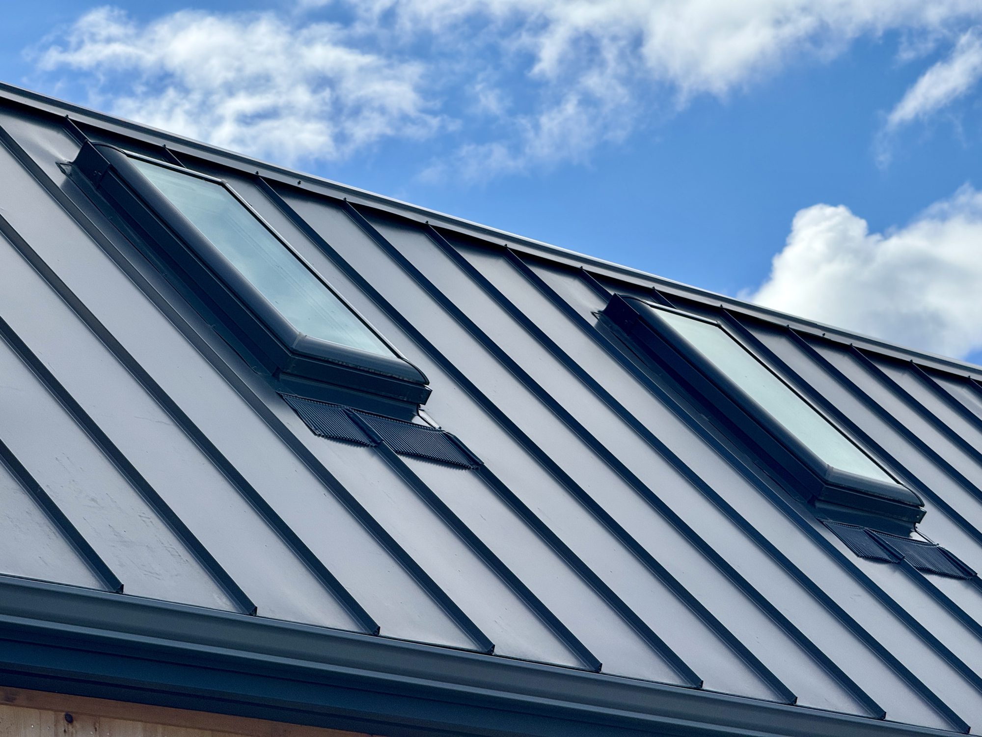 Closeup of attic window on house roof top covered with metal roof.