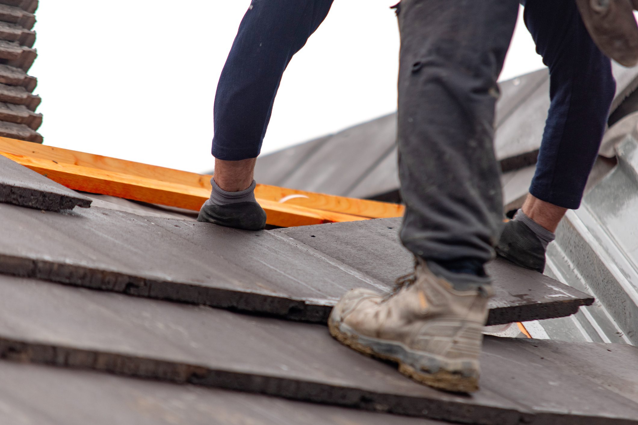 Roofer carefully places roof tiles on a sloped surface while standing on top of a building showcasing the effort involved in roofing work