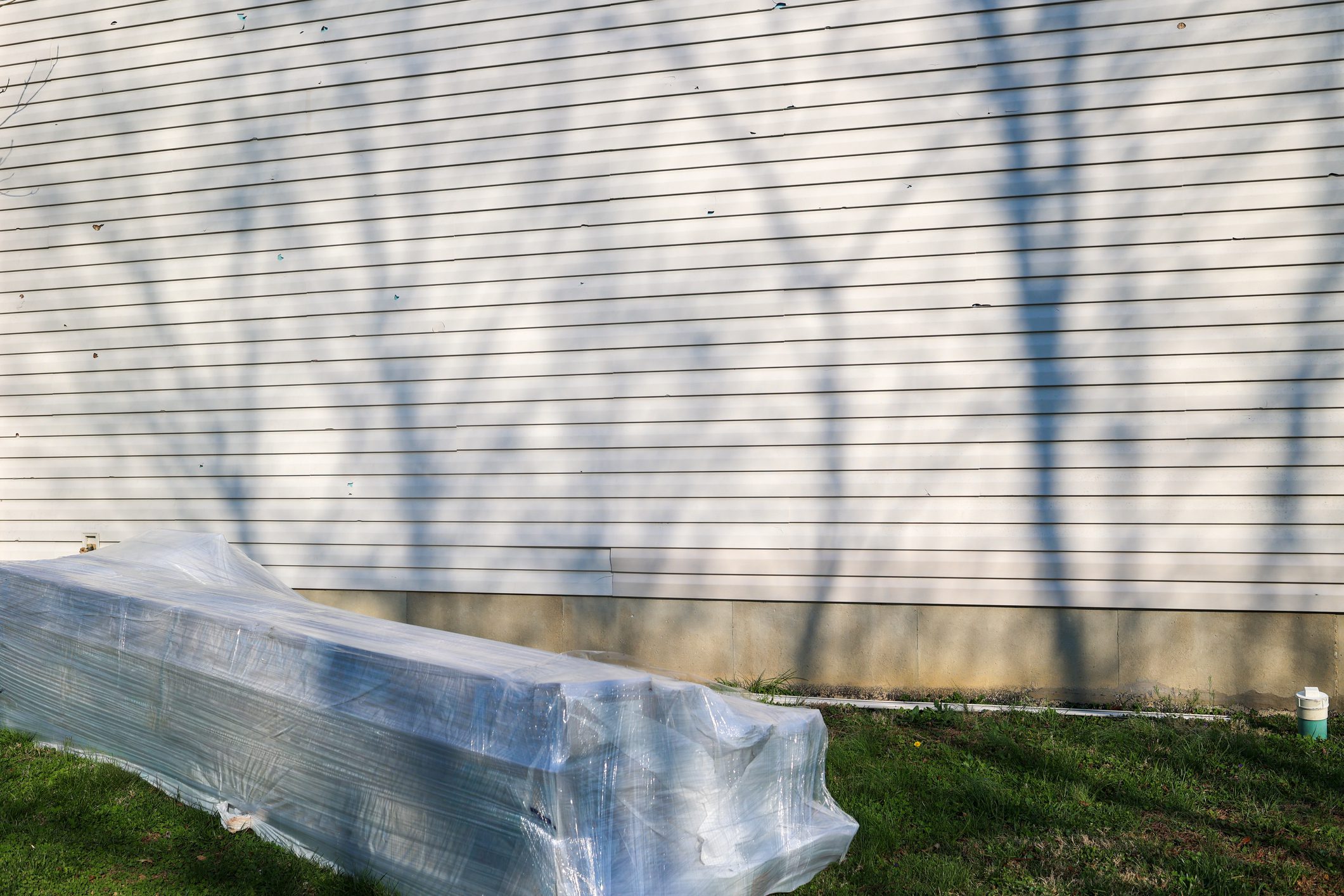 A stack of new vinyl siding next to a house for repairs