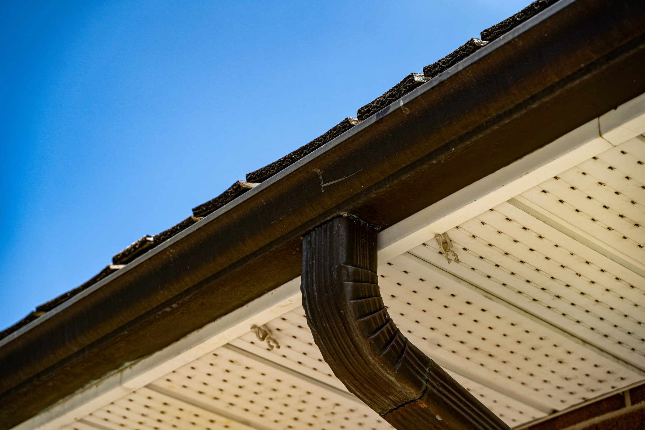 Close up of roof gutter and downspout under blue sky.