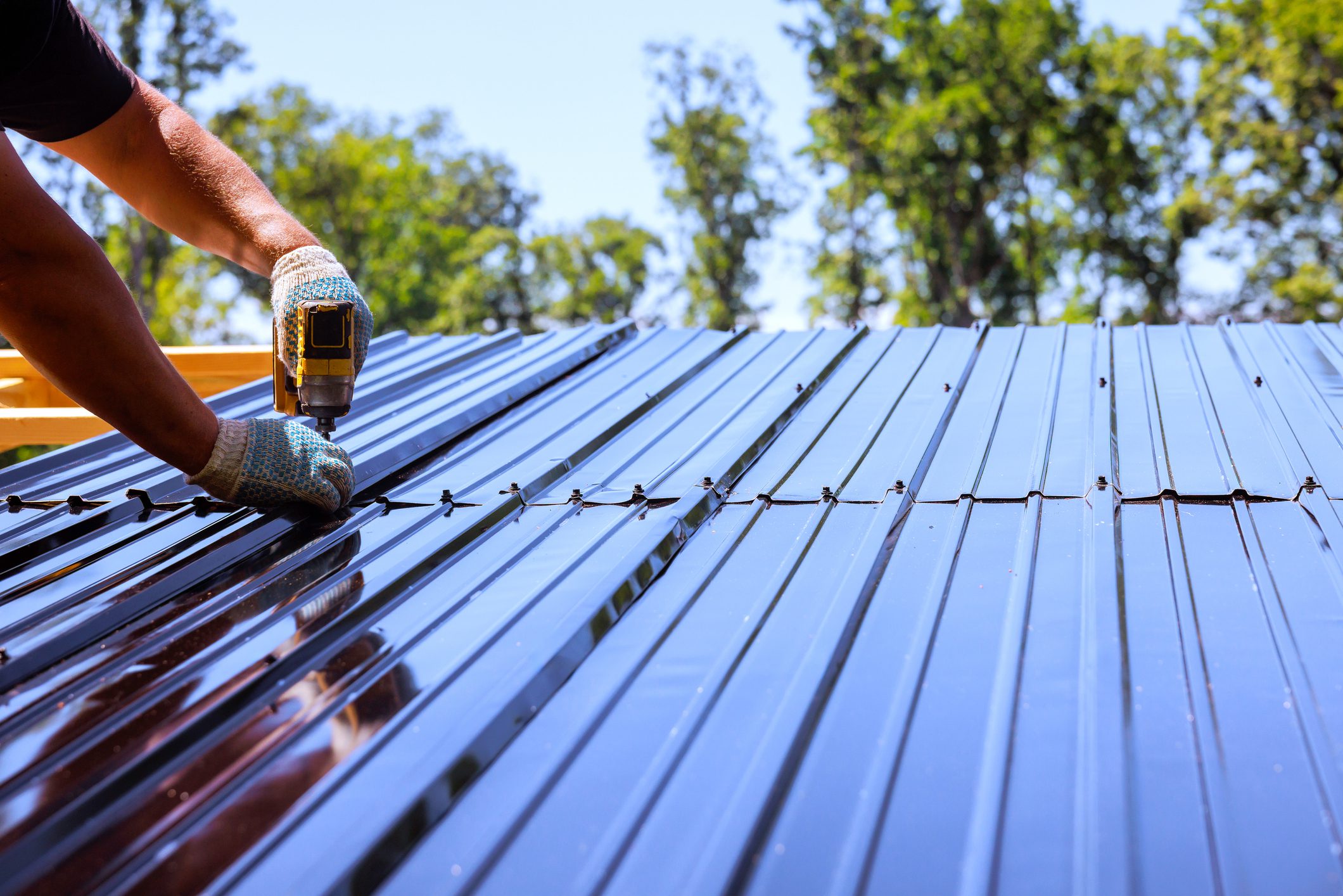 Contractor secures metal roofing sheets to house with power drill tool