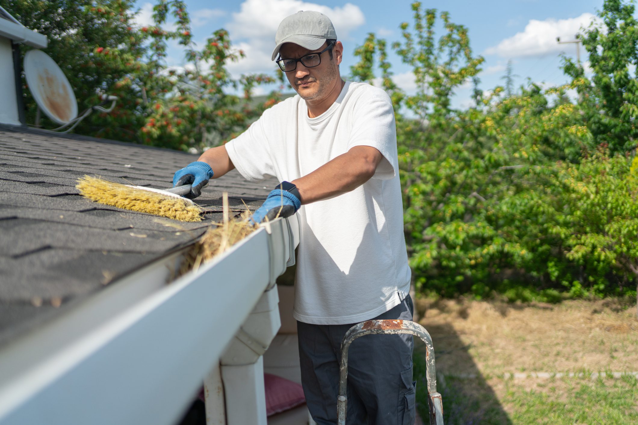 Worker On Ladder Cleaning House Rain Gutter