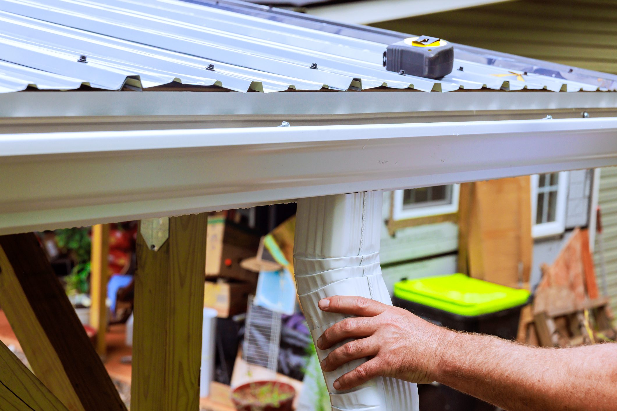 Contractor works on fitting gutter on metal roof while handling tools in residential area
