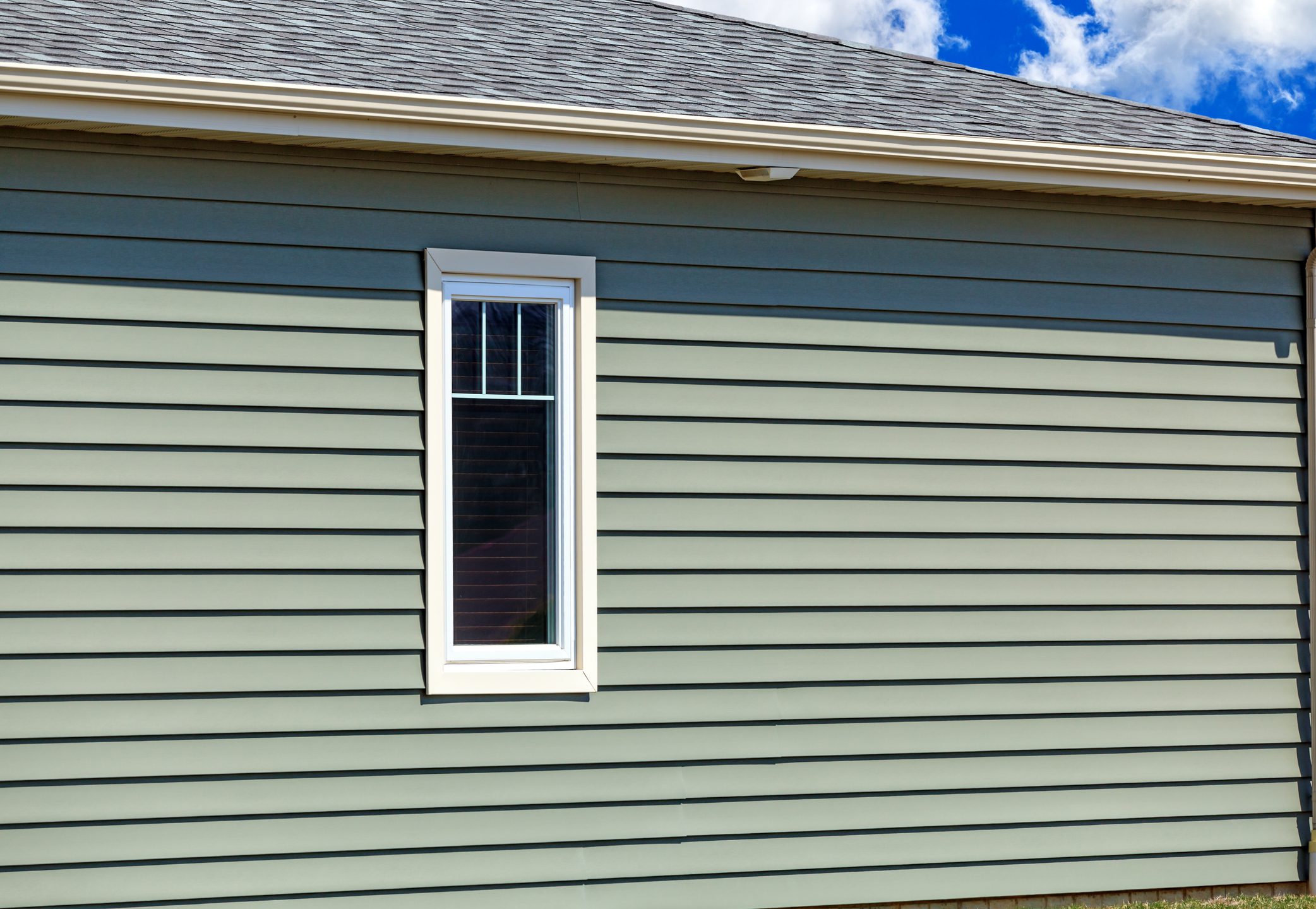 A cropped view of new vinyl siding, vinyl window, guttering and roofing.