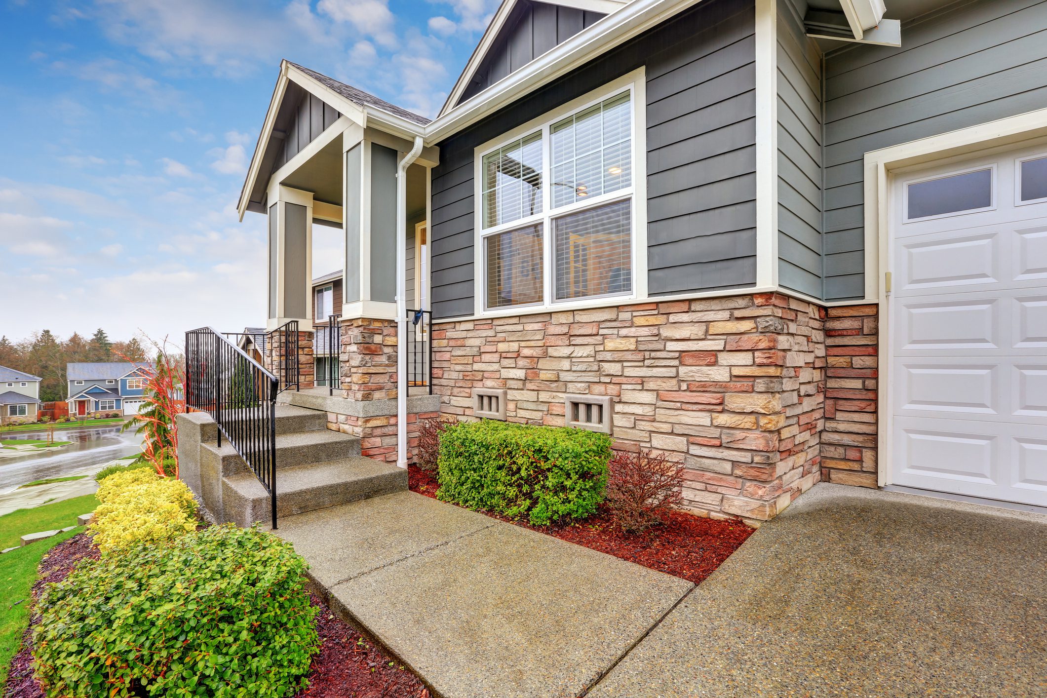 Gray house exterior with column porch and stone wall trim on a rainy day. Northwest, USA