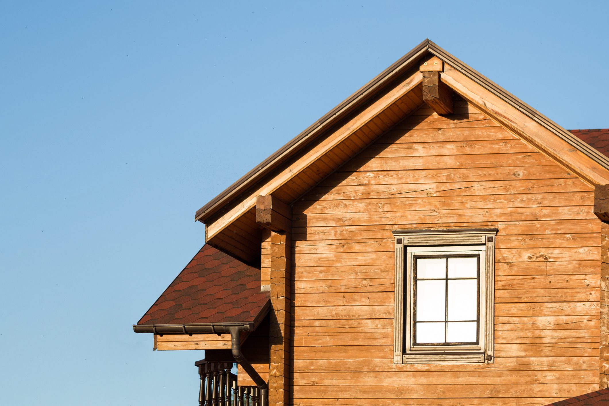 Part of modern wooden country house with blue sky on background. Roof of eco residential building near forest. Building and architecture of rustic chalet.