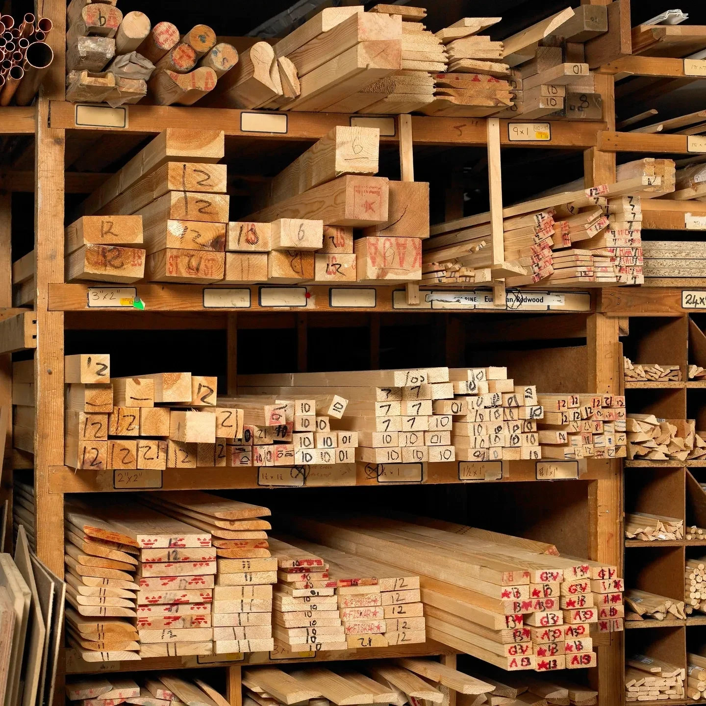 Wooden boards and dowels of various sizes are organized on shelves, each labeled for easy identification, reflecting a customer-first approach in this well-managed workshop or lumber storage area.