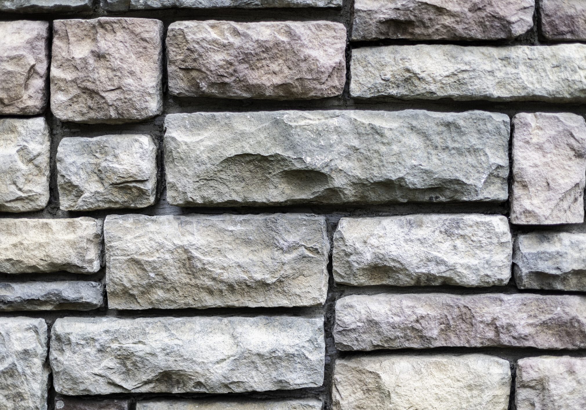 Close-up view of a stone wall made of rectangular, rough-hewn stones stacked in a horizontal pattern.