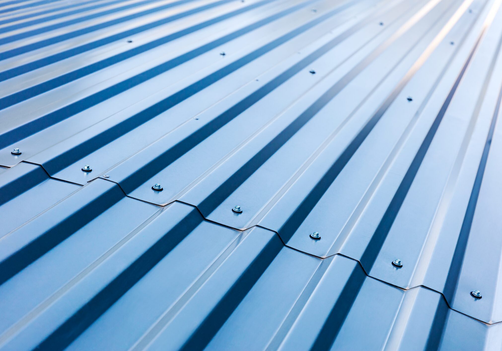 Close-up view of a blue corrugated metal roof with rivets securing the sheets in place, showing the texture and pattern of the roofing material.